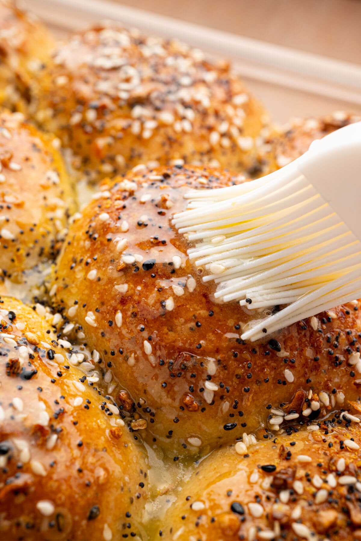 Brushing melted butter on a sourdough everything bagel roll.