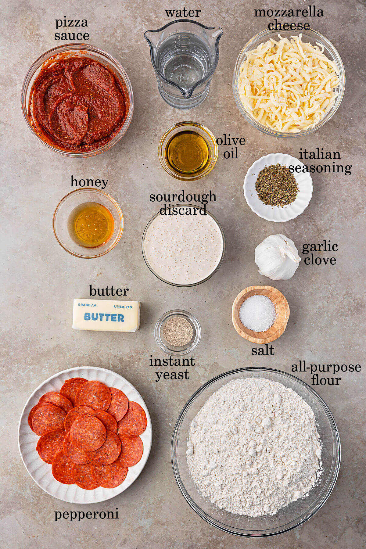 Ingredients for sourdough discard focaccia pizza in small bowls with text overlay labeling each ingredient.