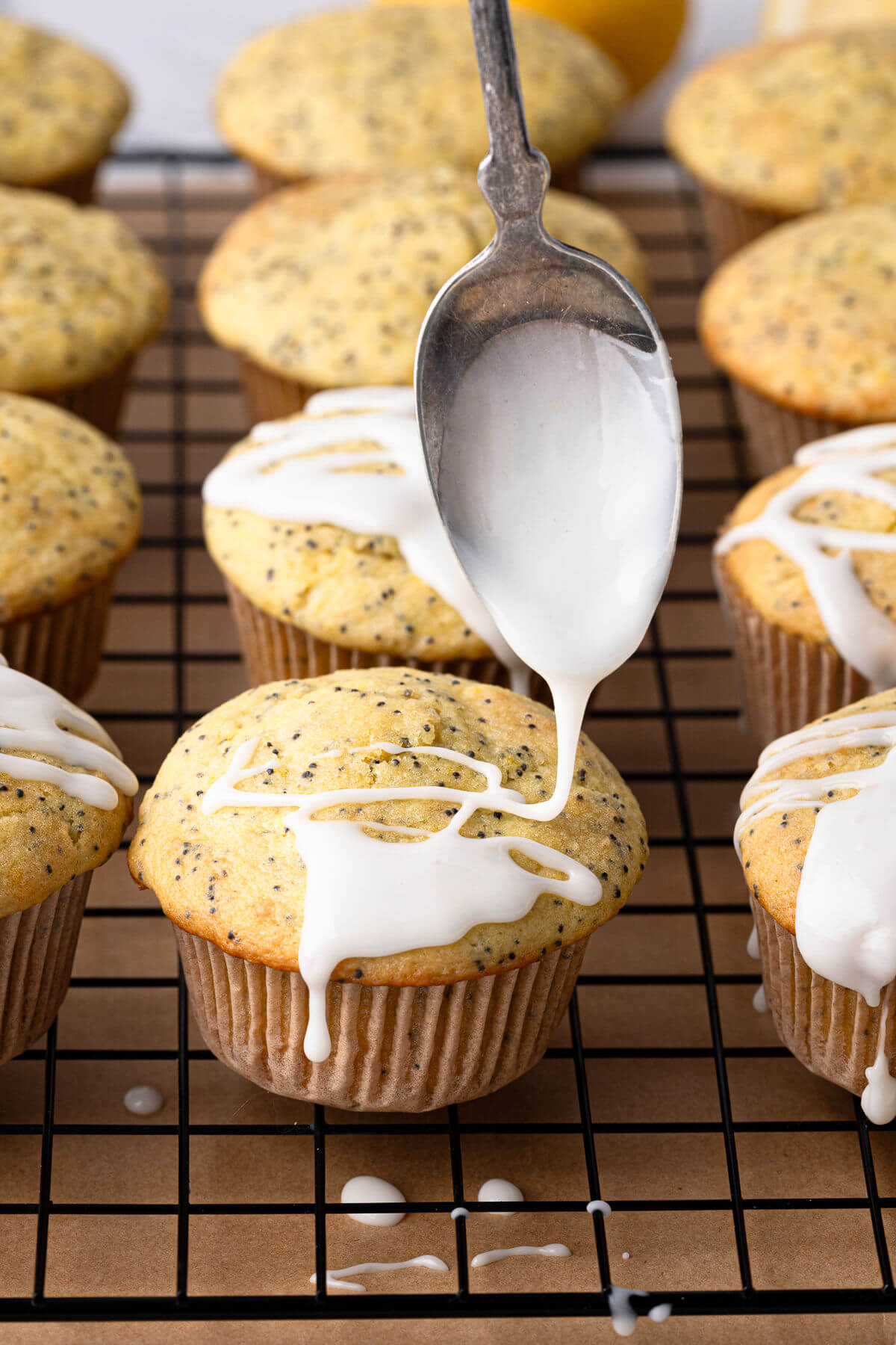 Spoon drizzling lemon glaze on sourdough lemon poppy seed muffins.