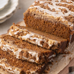 A loaf of sourdough discard pumpkin bread on a cutting board with three slices cut from the loaf.