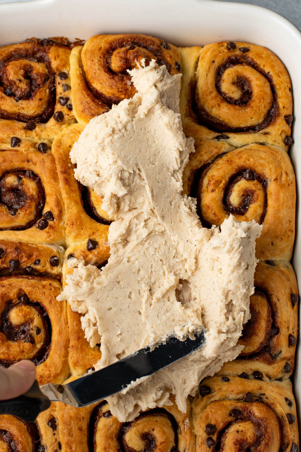 Spreading frosting on a pan of chocolate cinnamon rolls.
