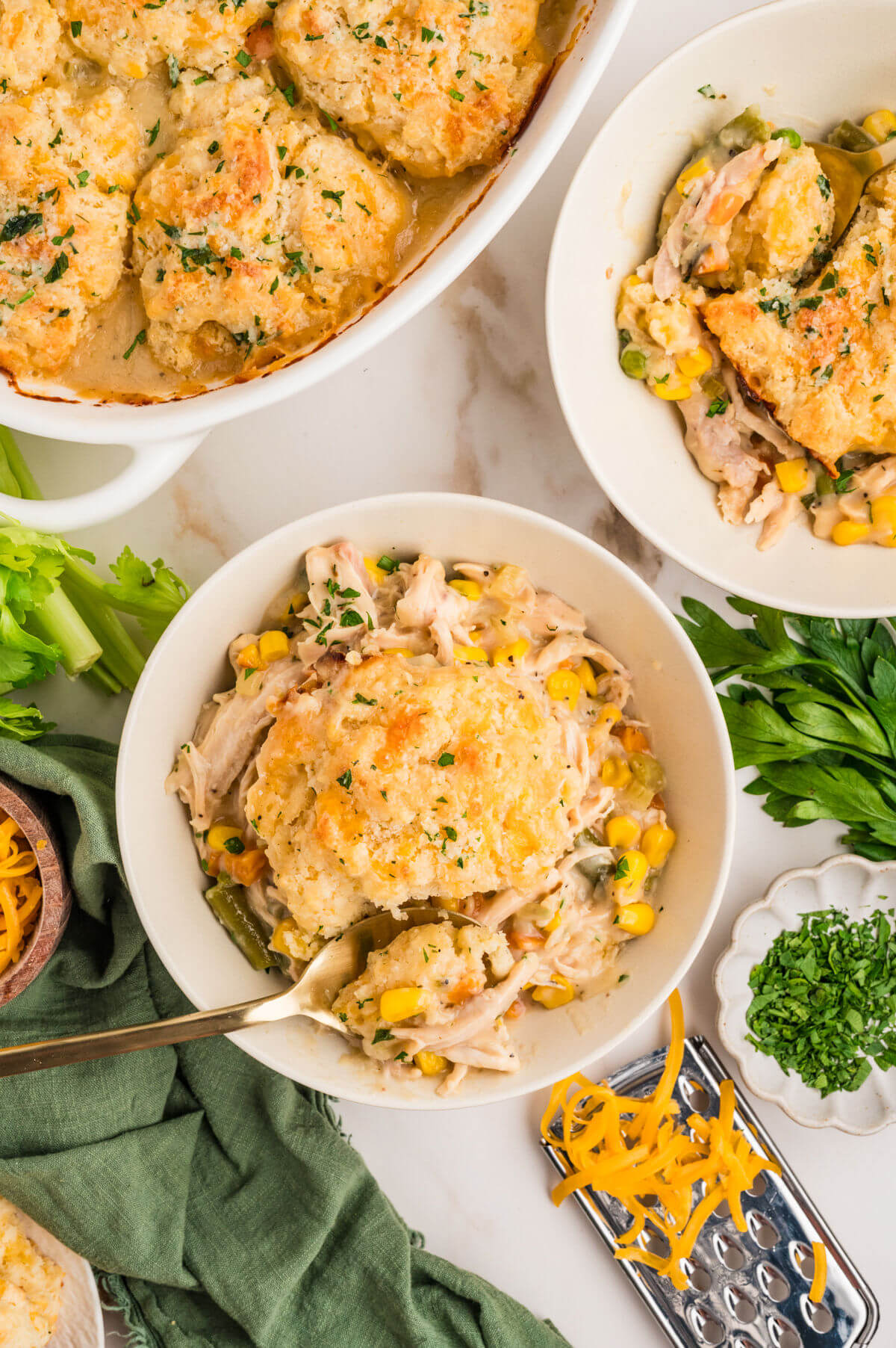 Turkey pot pie with biscuit topping in a casserole dish and in two serving bowls.