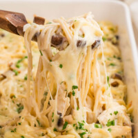 Turkey tetrazzini in a baking dish being served with a wooden spoon.