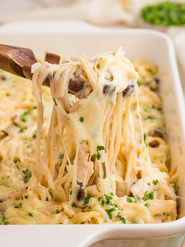 Turkey tetrazzini in a baking dish being served with a wooden spoon.