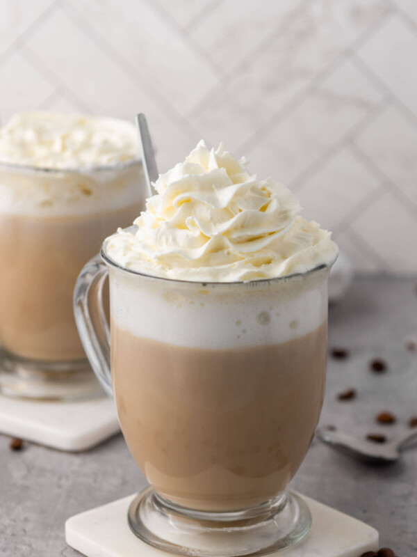 Two vanilla lattes in glass mugs sitting on coasters.