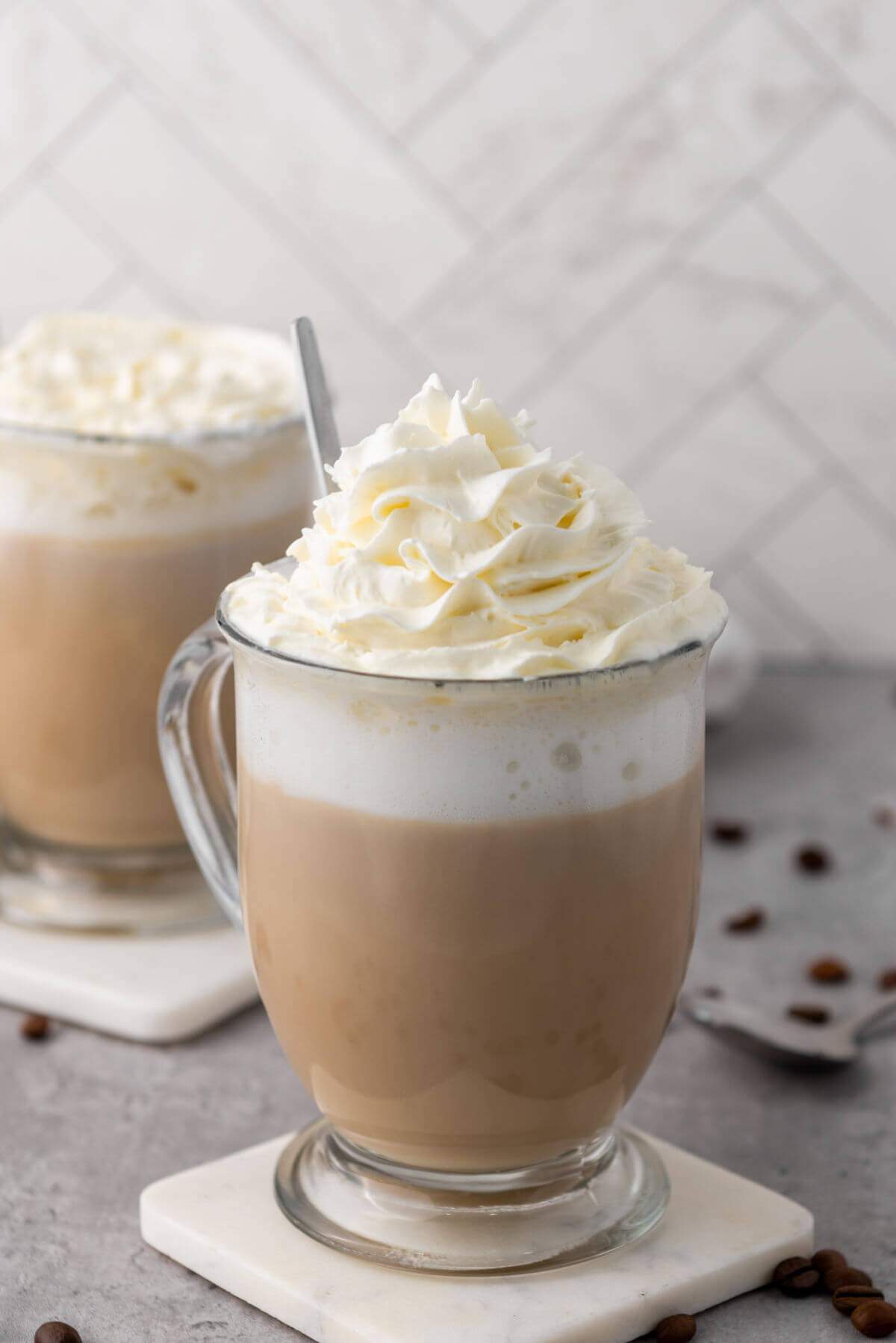 Two vanilla lattes in glass mugs sitting on coasters.