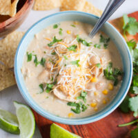Bowl of crockpot white chicken chili with lime slices and corn chips.