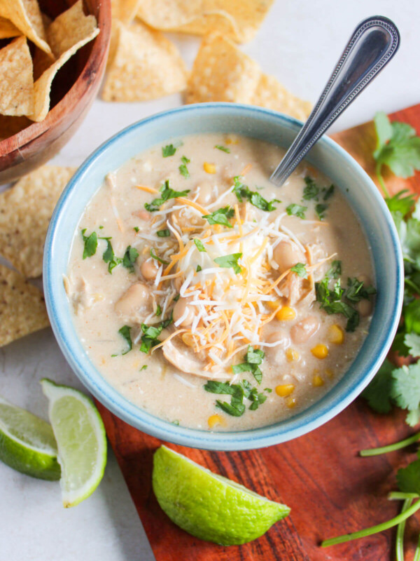 Bowl of crockpot white chicken chili with lime slices and corn chips.