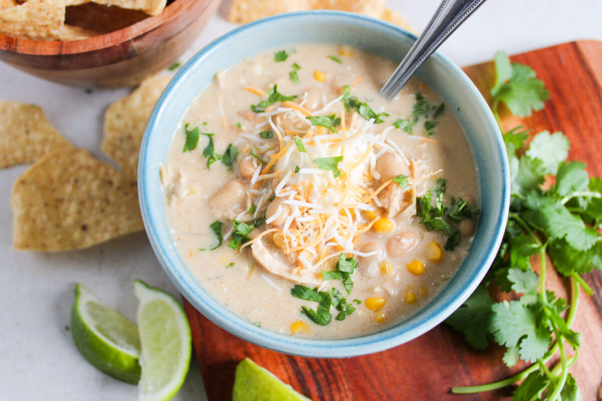 crockpot white chicken chili in a bowl with tortilla chips, lime wedges, and parsley.