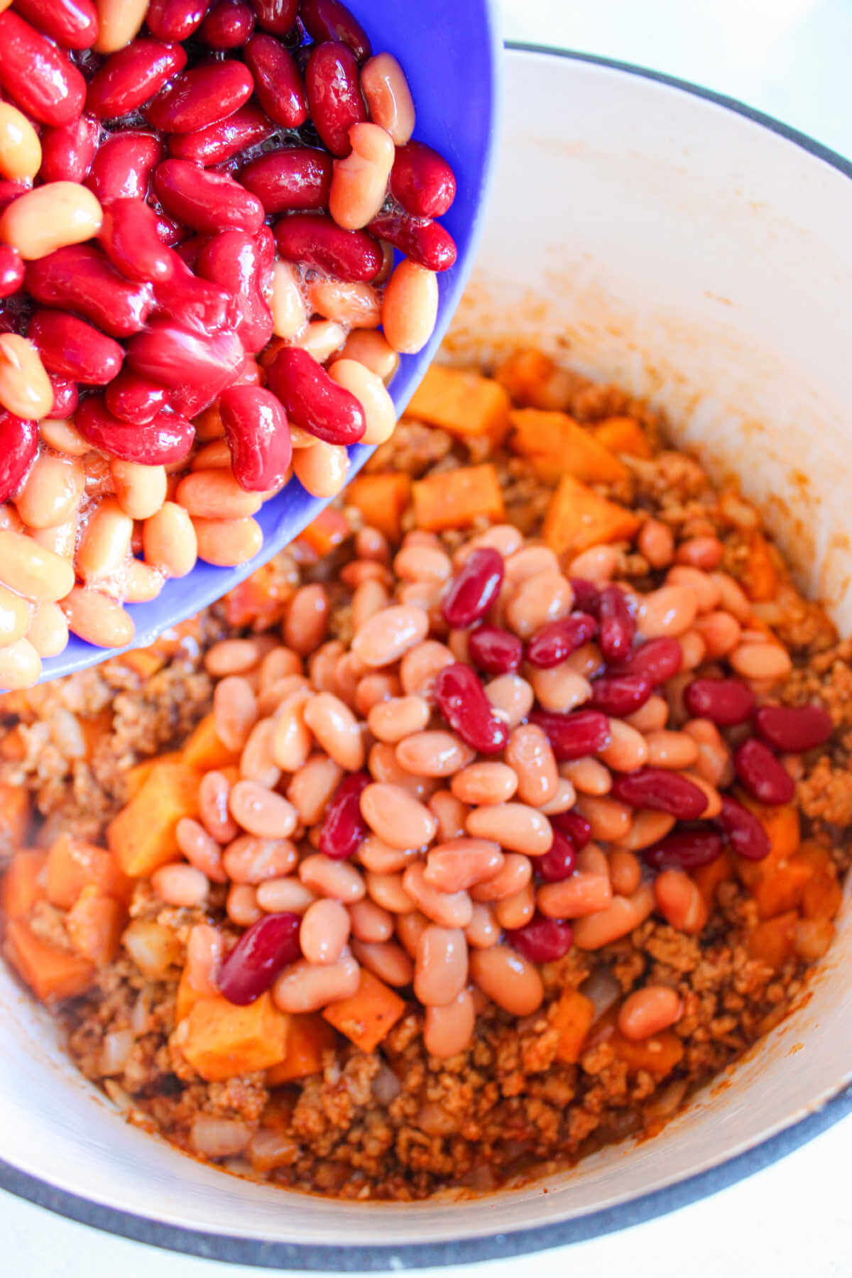 Adding beans to chicken chili with sweet potatoes.