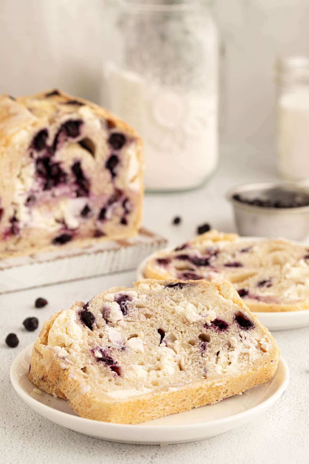 blueberry cream cheese sourdough bread loaf in background and slice of bread on a white plate