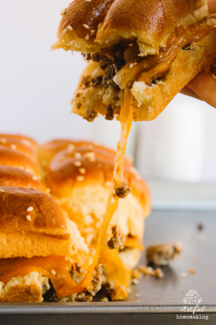 hand pulling a cheeseburger slider out of pan