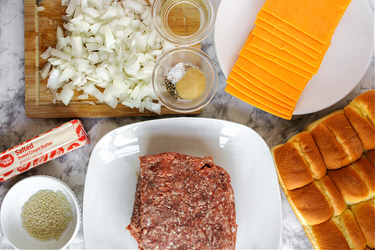 ingredients on a marble countertop: ground beef, hawaiian rolls, butter, onion, and cheese slices