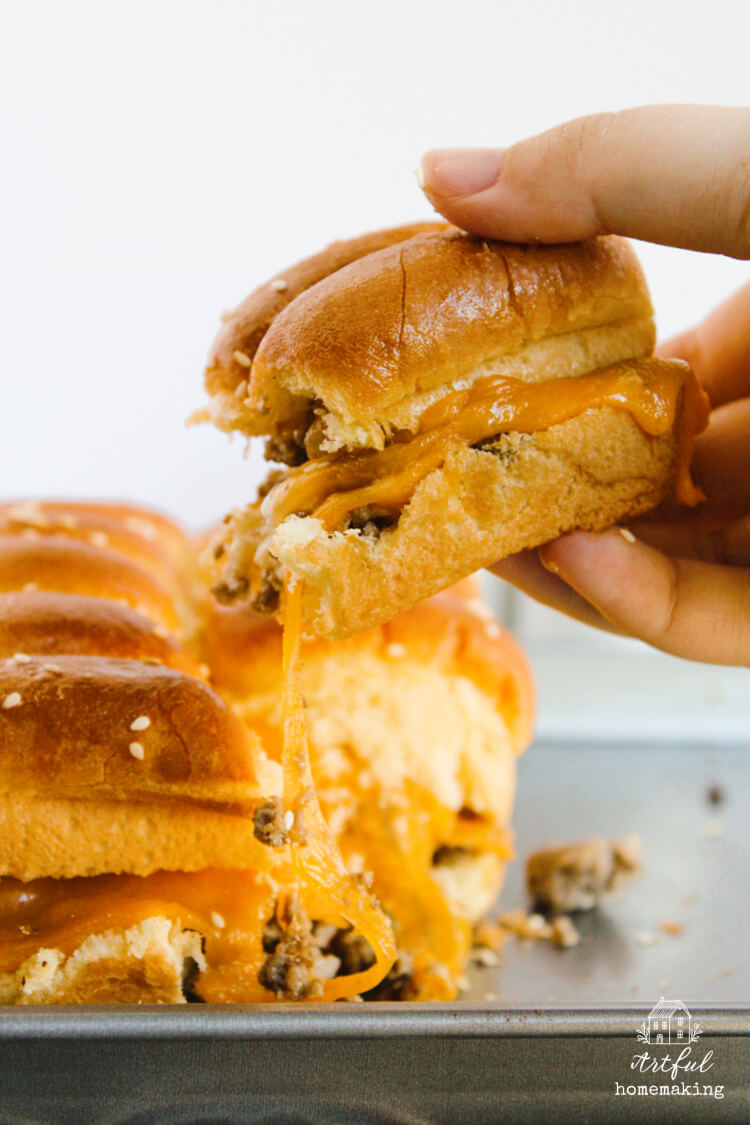 hand pulling a cheeseburger slider from the pan with cheese stretching
