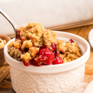 small white bowl next to a white baking dish filled with cherry crumble