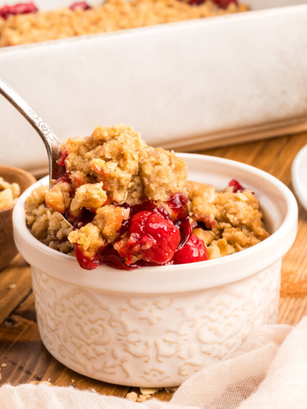 small white bowl next to a white baking dish filled with cherry crumble