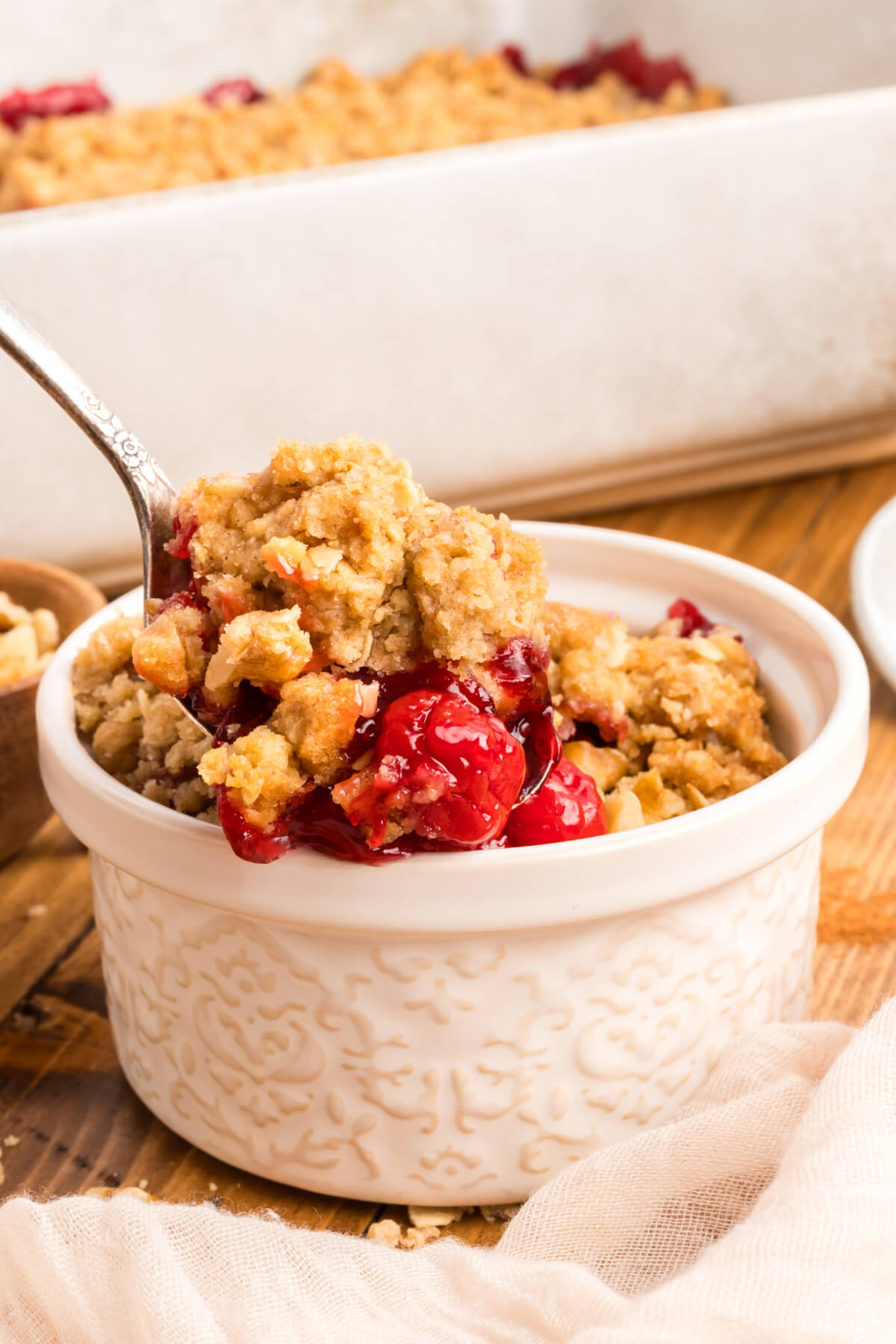 small white bowl next to a white baking dish filled with cherry crumble