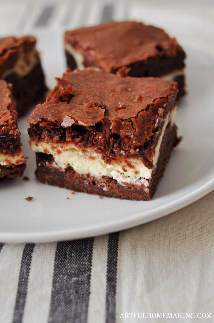 cream cheese brownies on a white plate sitting on a striped linen tablecloth