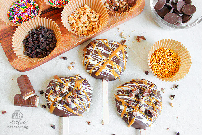 chocolate covered apples on sticks laying on a white counter top with various candy toppings