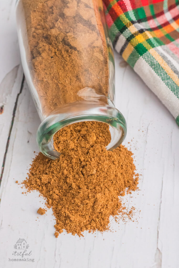 christmas spice mix spilling out of clear glass jar onto wooden tabletop