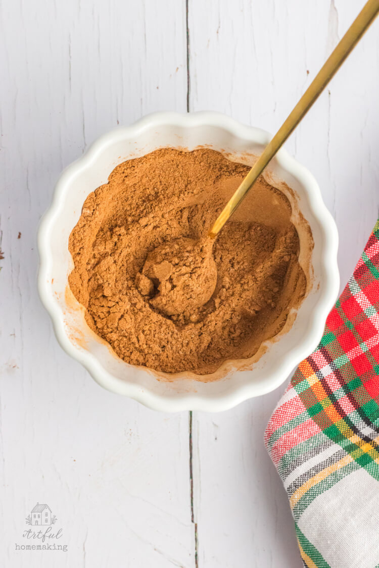 christmas spice mix in a white bowl with a gold spoon mixing it together