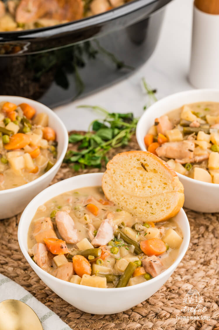 three white bowls of chicken stew sit next to a slow cooker