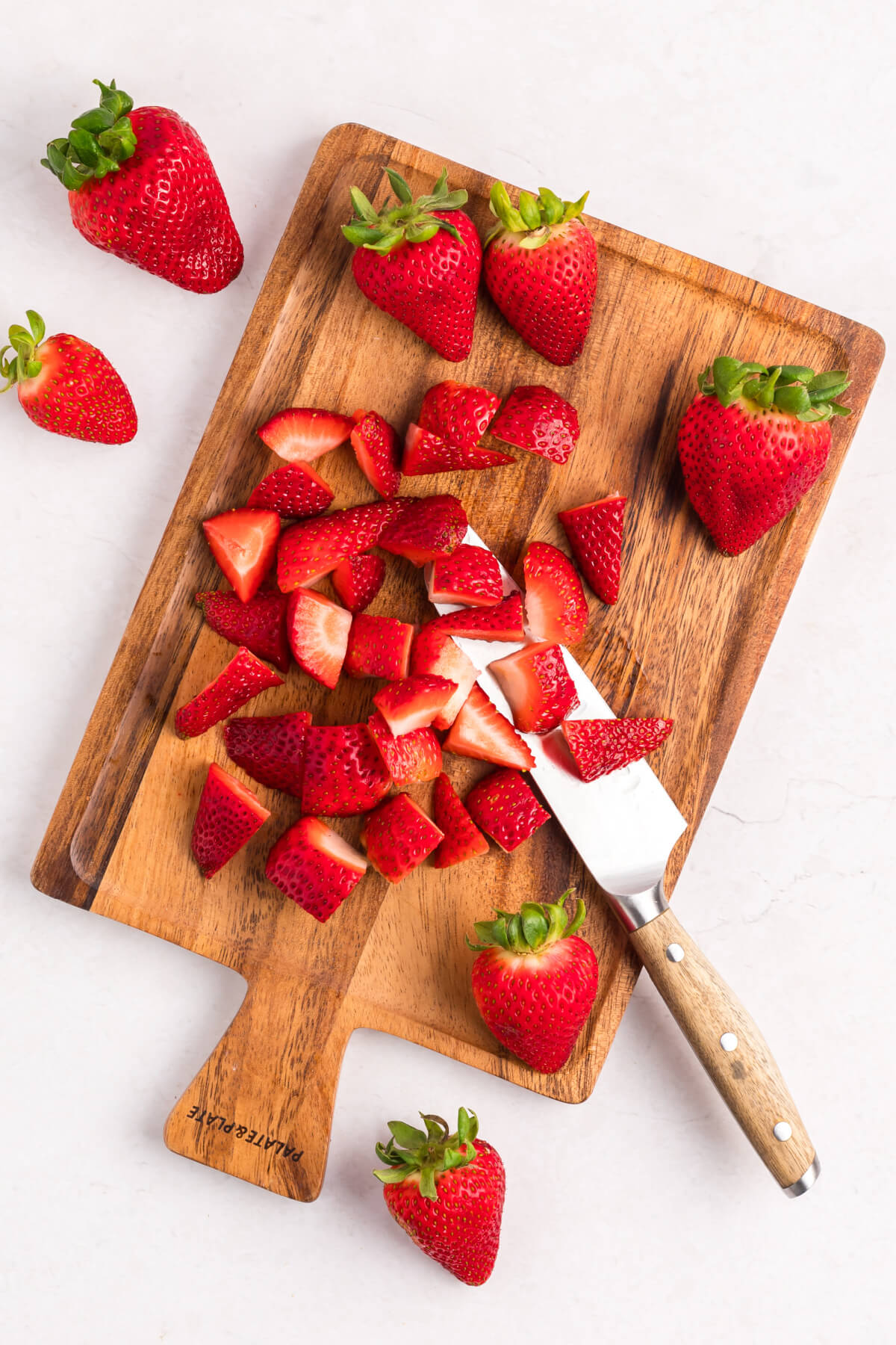 top down view of strawberries being chopped on a wooden cutting board with a knife