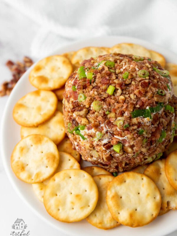 a bacon pecan cheeseball on a white plate surrounded by round crackers