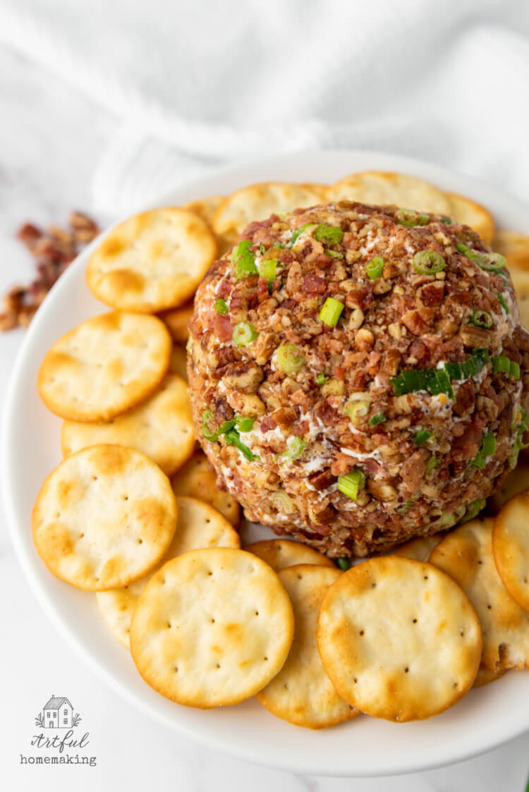 a bacon pecan cheeseball on a white plate surrounded by round crackers