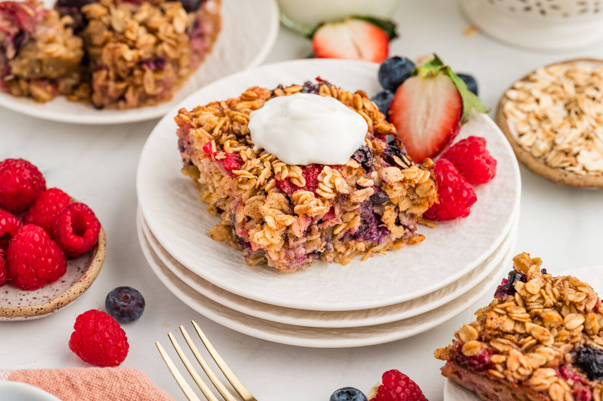 Slice of baked oatmeal on a plate with whipped cream on top and berries next to it.