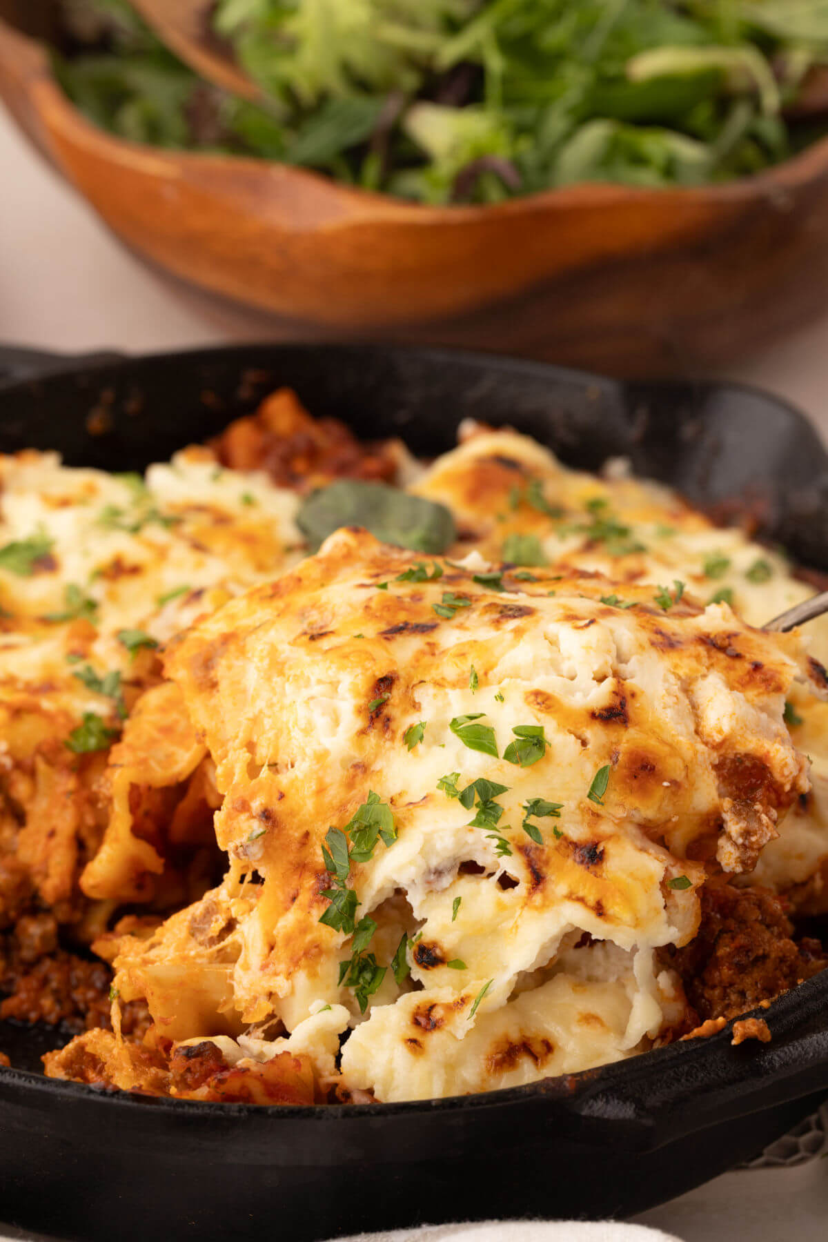 A piece of cheesy skillet lasagna being lifted out of a cast iron skillet after baking.