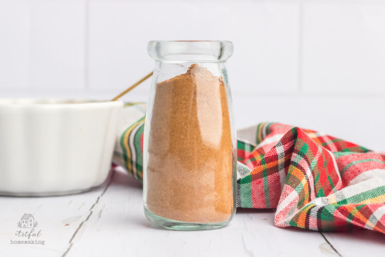 glass jar of spice mix on a white wood table next to a white bowl