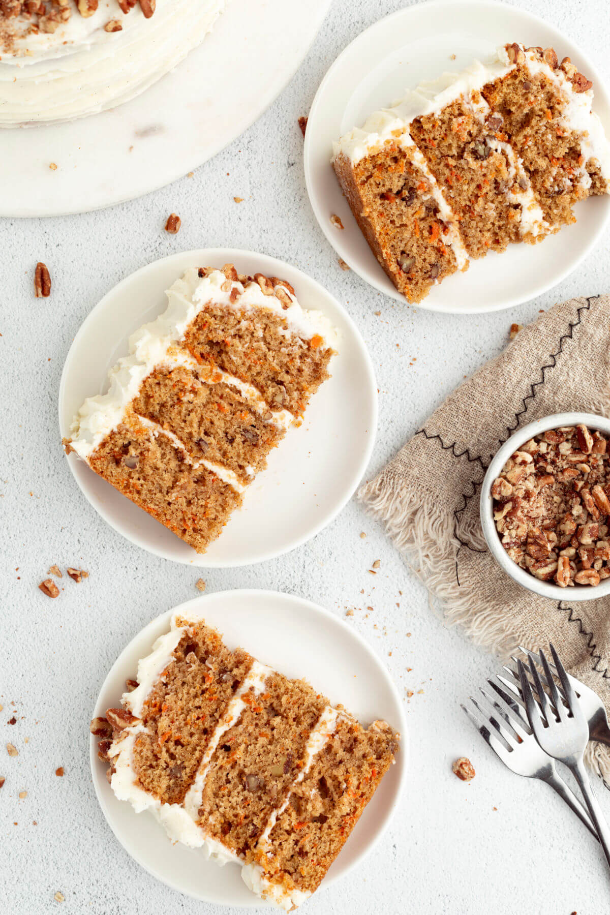 Three slices of sourdough carrot cake on three white plates next to a pile of forks.