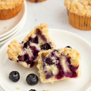 Sourdough blueberry muffin cut open on a plate with a few fresh blueberries next to it.