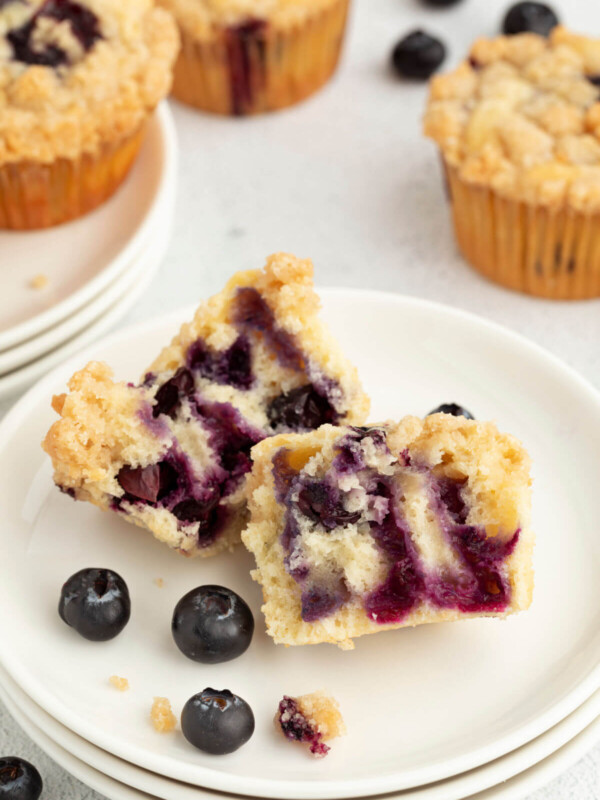 Sourdough blueberry muffin cut open on a plate with a few fresh blueberries next to it.