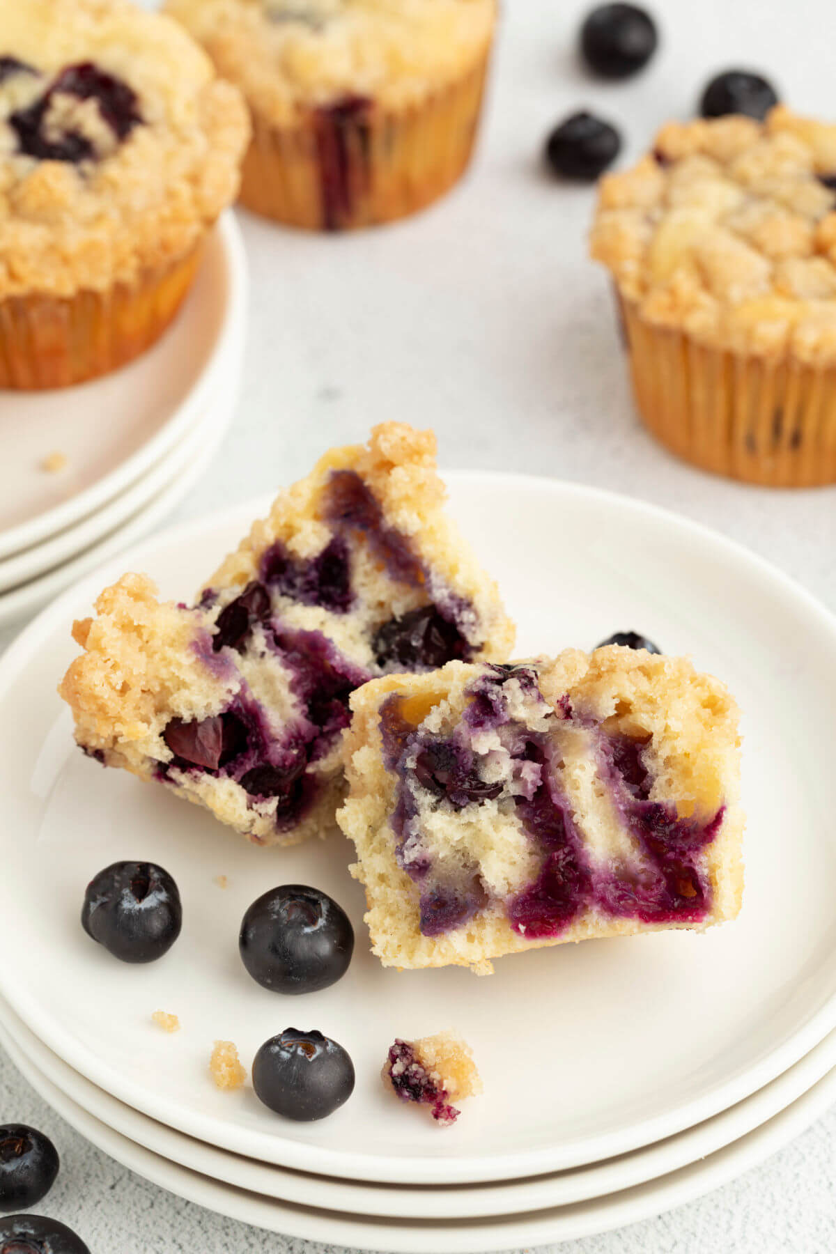 Sourdough blueberry muffin cut open on a plate with a few fresh blueberries next to it.