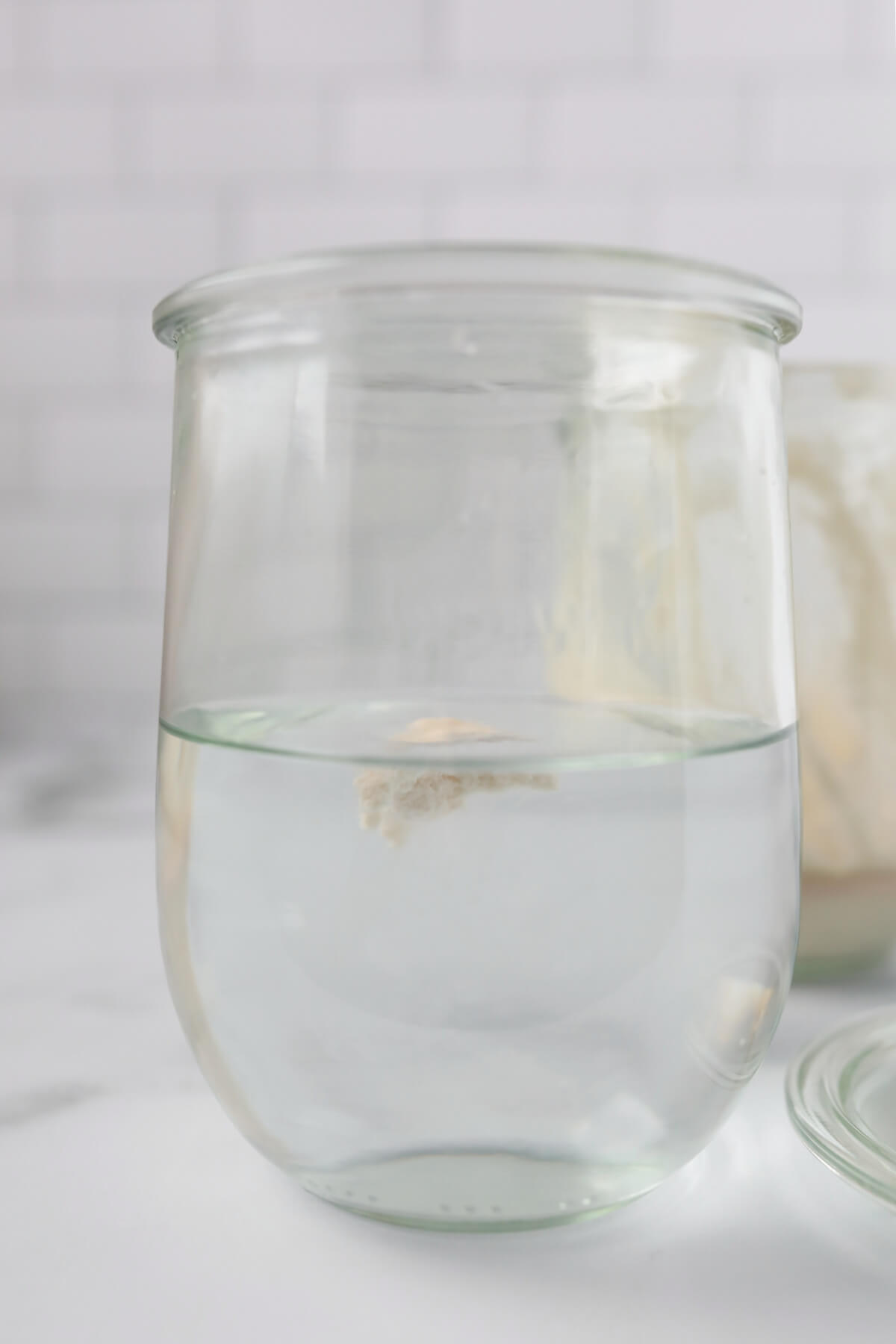Glass jar of water with a spoonful of sourdough starter floating in the water showing how to do the float test.