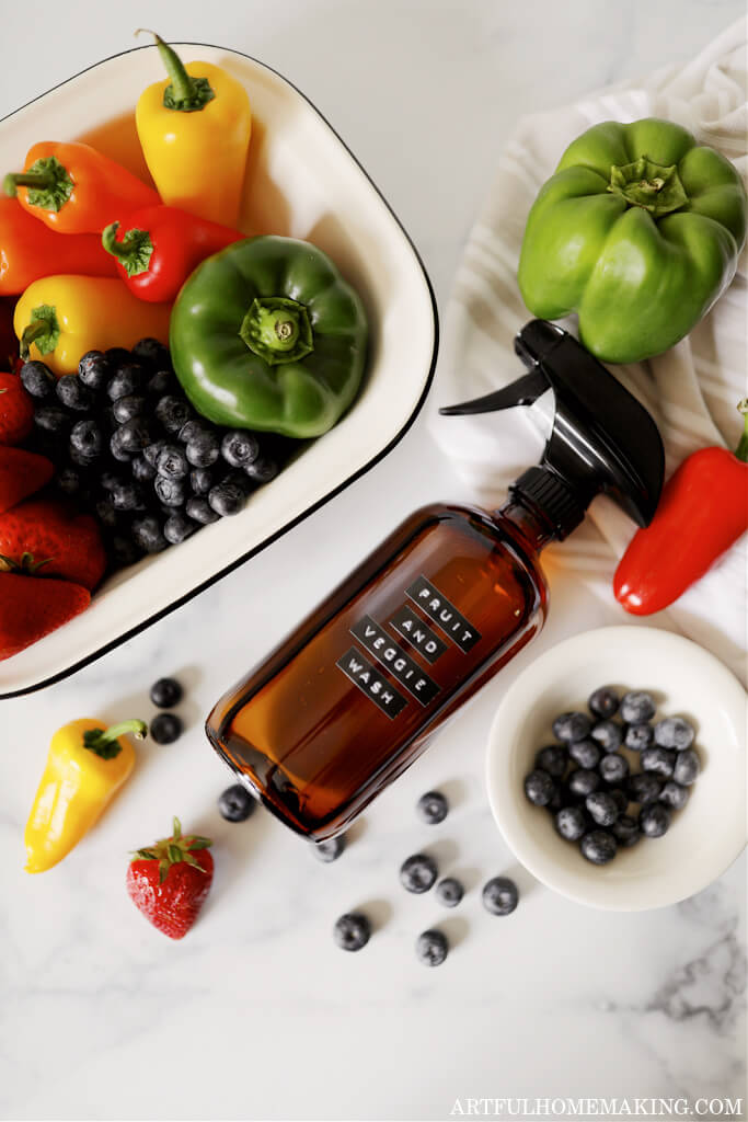 amber spray bottle with fruit and vegetable wash spray laying on a kitchen counter surrounded with fruit and vegetables
