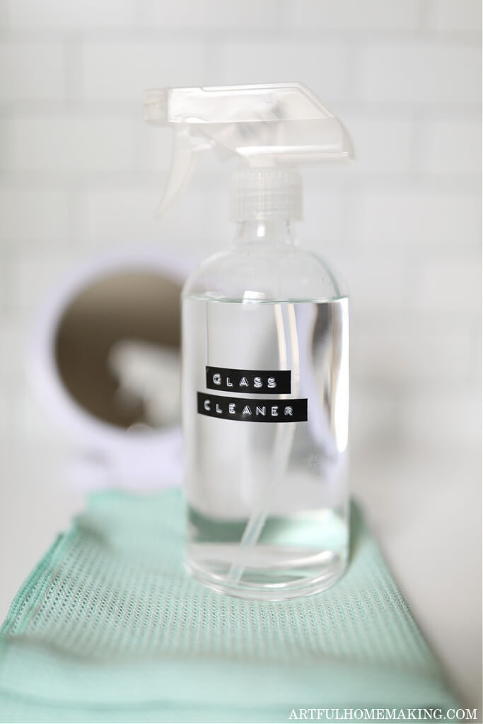 glass cleaner in a glass spray bottle on a marble countertop next to a small mirror