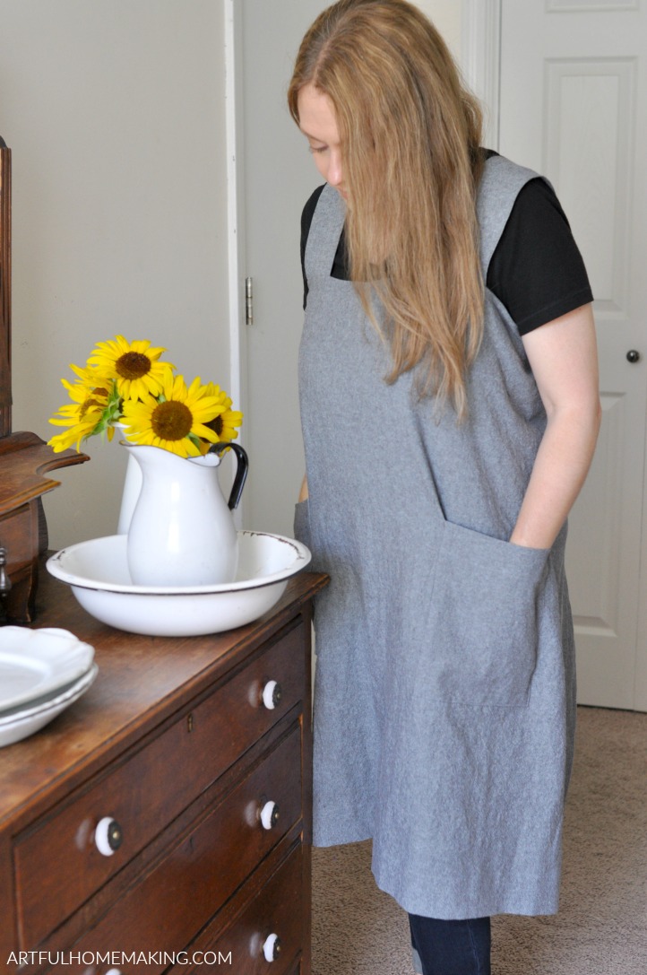 woman with hand in apron pocket next to sunflowers in white pitcher