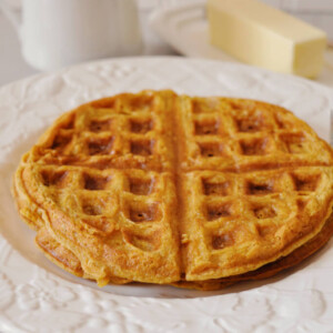 Two whole wheat healthy pumpkin waffles on a plate with maple syrup and butter.