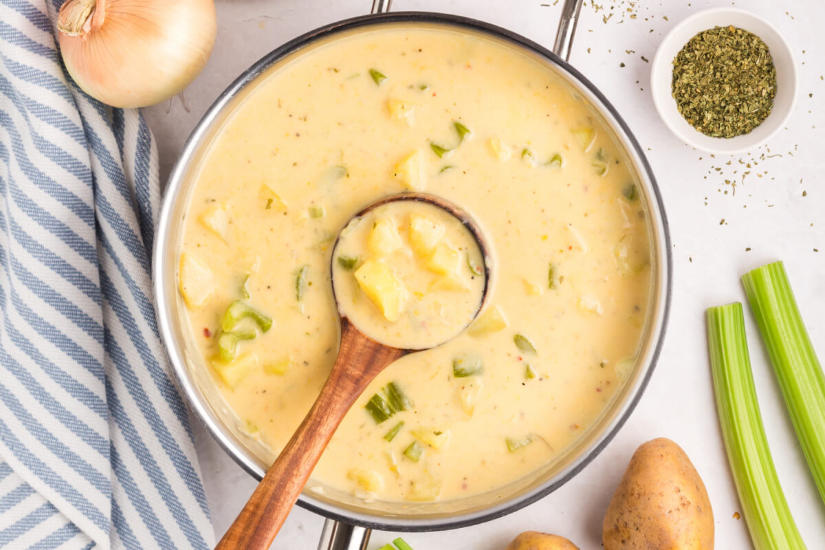 top down view of a soup pot with cheesy potato soup and a wooden ladle