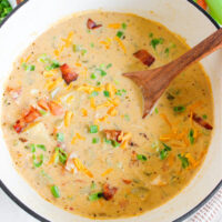 a white bowl filled with homemade chicken potato soup with a wooden spoon