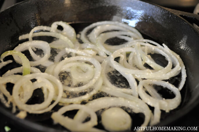 sliced onion rings frying in coconut oil in a cast iron skillet