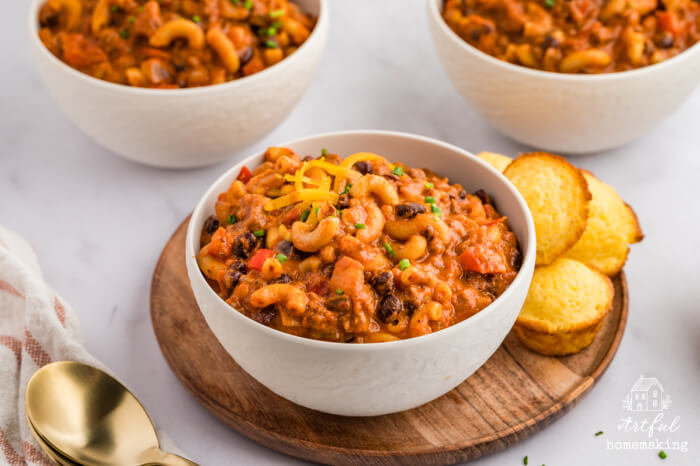 chili mac in white bowl with cornbread muffins on a wooden plate