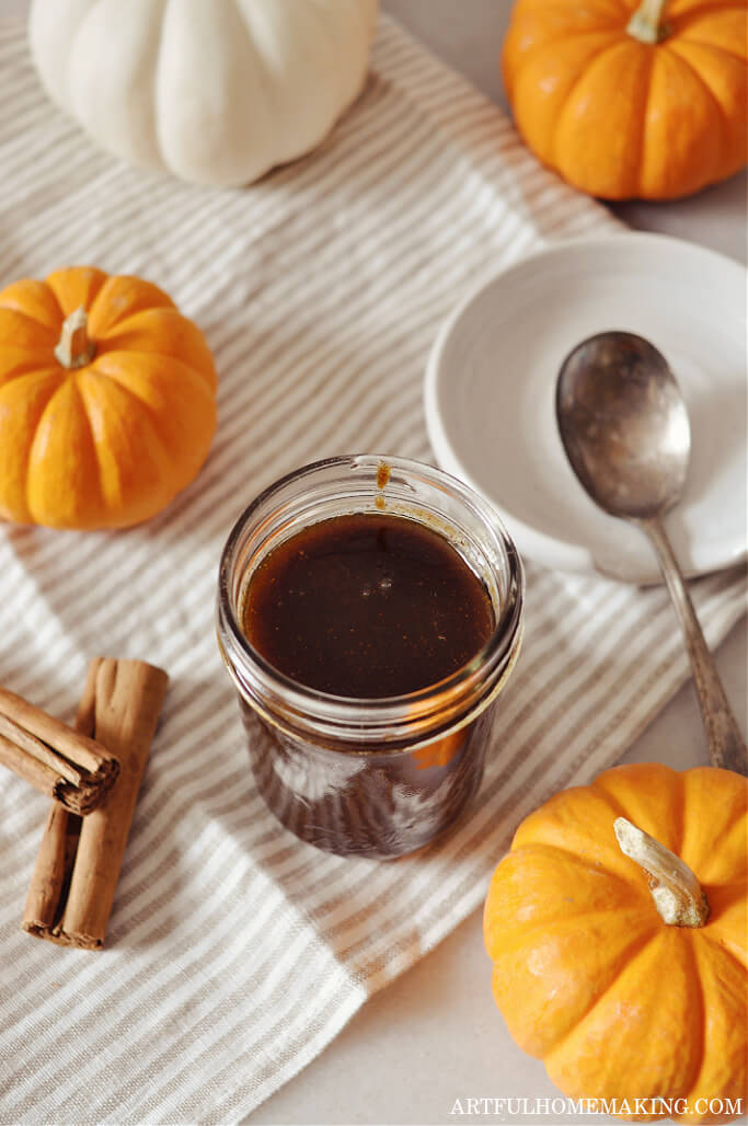 pumpkin spice coffee syrup in a jar with orange and white pumpkins and cinnamon sticks on table