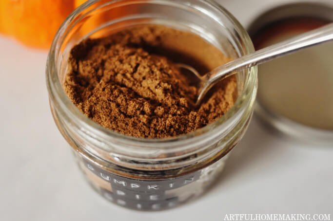 pumpkin pie spices being added to glass mason jar with a spoon