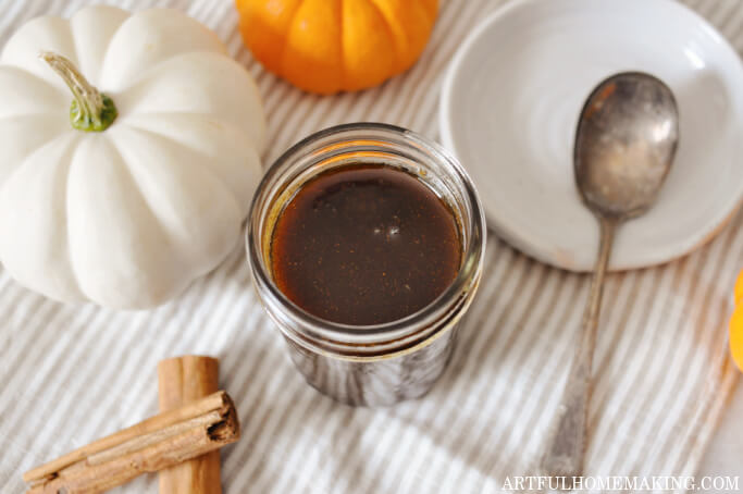 pumpkin spice coffee syrup in a jar with pumpkins and cinnamon sticks surrounding it