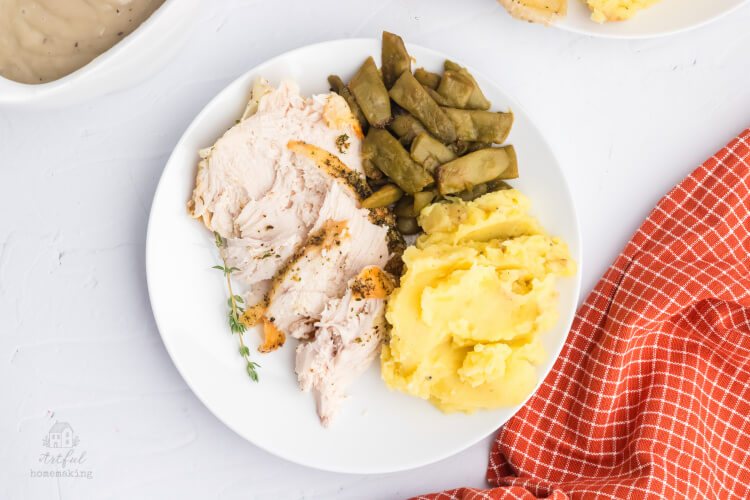 white plate with sliced chicken, mashed potatoes and green beans