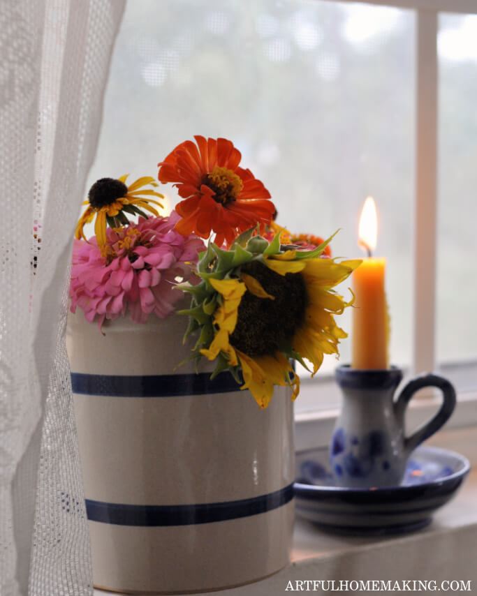 pottery vase with blue stripes filled with flowers on a windowsill next to a candle